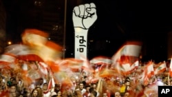 FILE - Protesters wave Lebanese flags during an anti-government protest in Beirut, Lebanon, Nov. 10, 2019. The Arabic writing beneath the fist reads "Revolution."