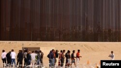 Sejumlah migran berkumpul di dekat tembok perbatasan AS-Meksiko setelah berhasil berhasil menyeberangi sungai Rio Bravo di area perbatasan kedua negara. Foto diambil dari wilayah Ciudad Juarez, Meksiko, pada 5 Oktober 2023. (Foto: Reuters/Jose Luis Gonzalez)