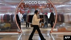 一名女子走过北京一个商场内的一家挂满冬衣的服装店。（2024年12月3日）