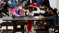 FILE - Migrants pass the time at a migrant shelter, May 12, 2021, in McAllen, Texas. Migrants from four countries were among those who rode a bus from Texas to Washington, D.C., that arrived Wednesday.