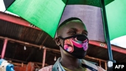 Seorang penjual di pasar Nakasero di Kampala memakai masker wajah sambil memegang payung pada 1 April 2020. (Foto: AFP)