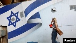 Seorang perempuan berjalan melewati mural bendera Israel, di tengah konflik yang sedang berlangsung di Gaza antara Israel dan Hamas, di Tel Aviv, Israel, 10 November 2024. (Foto: AFP)