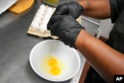 Johkiya Pierre cracks eggs while preparing an omelet at The Breakfast Brothers restaurant, Feb. 12, 2025, in Arlington, Texas.